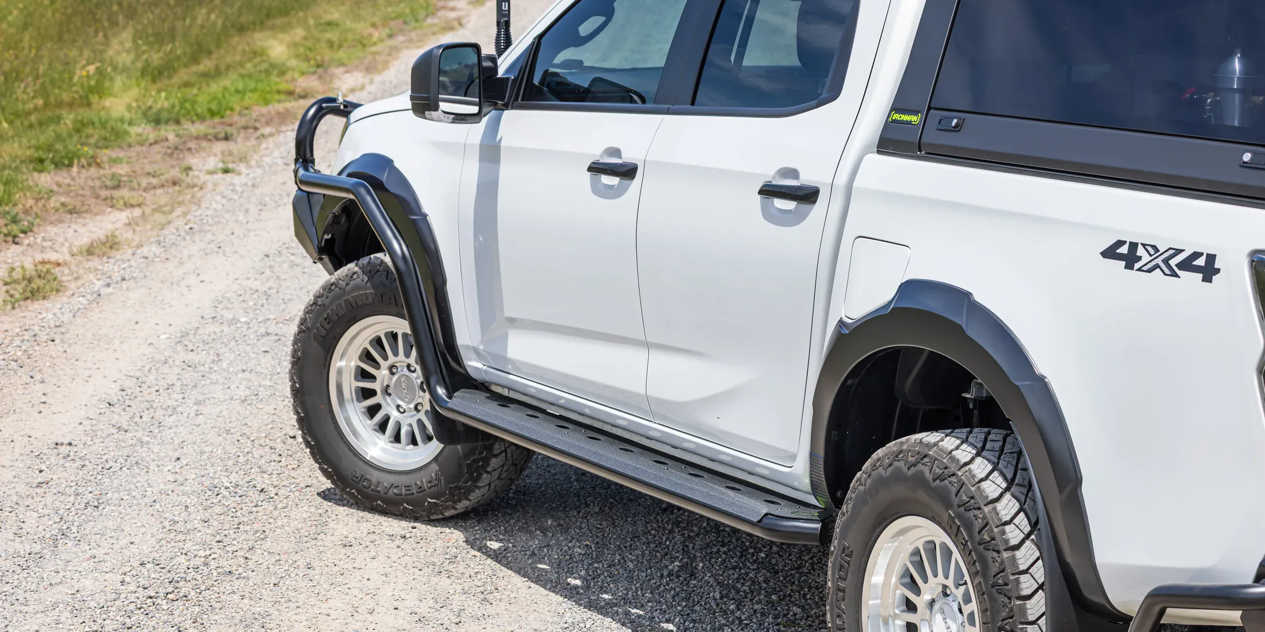A white dual cab ute fitted with a bull bar, side steps, guard flares and a canopy on a gravel track