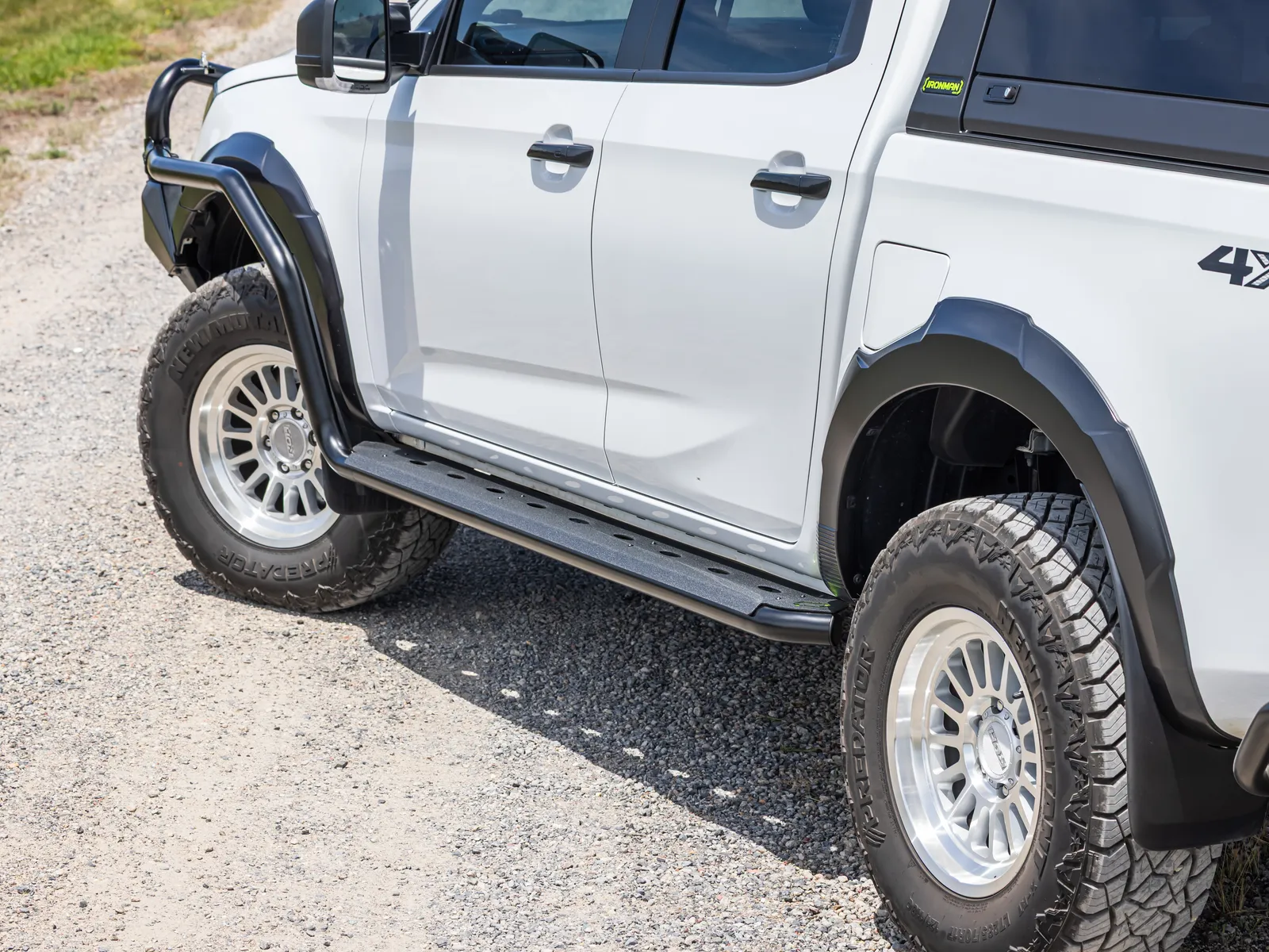 Side steps, guard flares and alloy wheels on a white dual cab ute parked on gravel