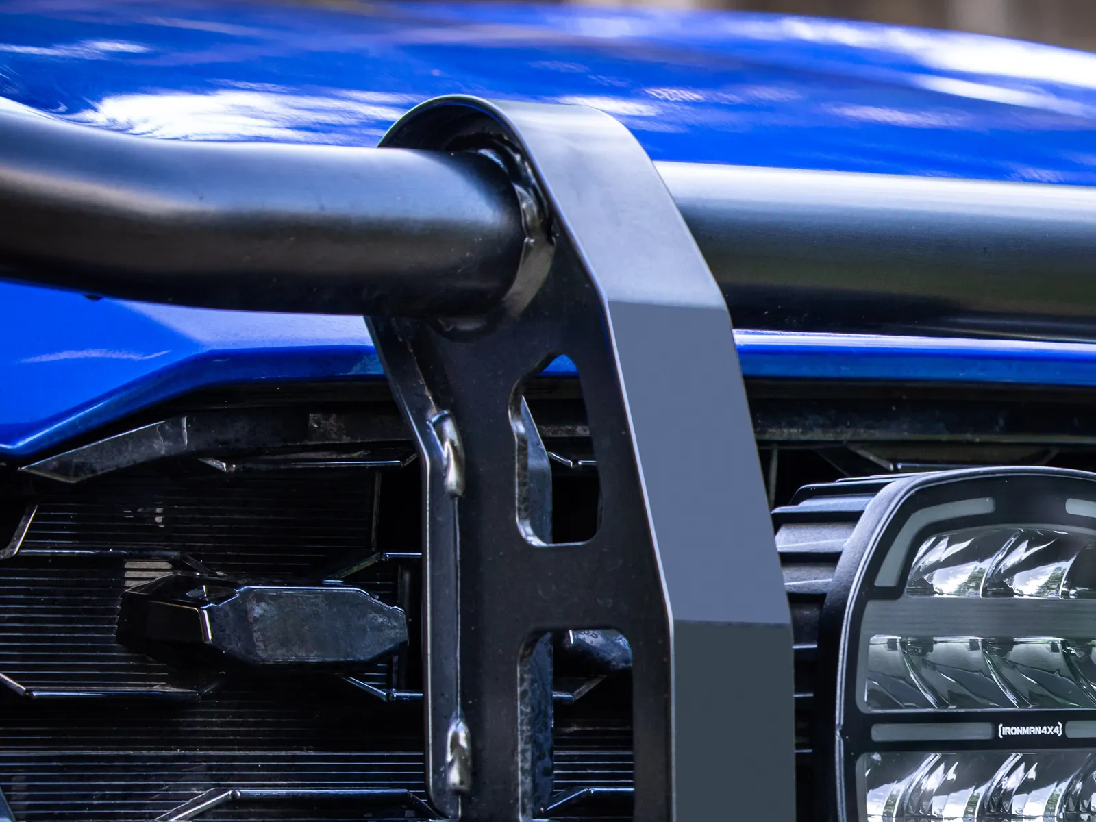 An IRONMAN 4X4 driving light mounted behind the upright of a black bull bar