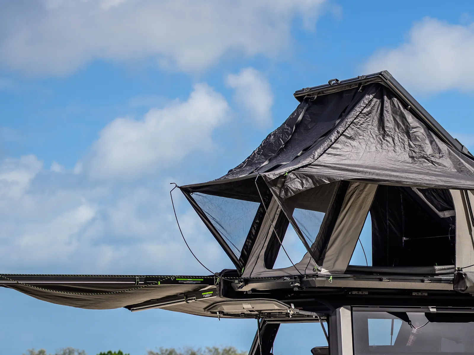 An IRONMAN 4X4 rooftop tent set up on a roof platform, with a folded awning alongside