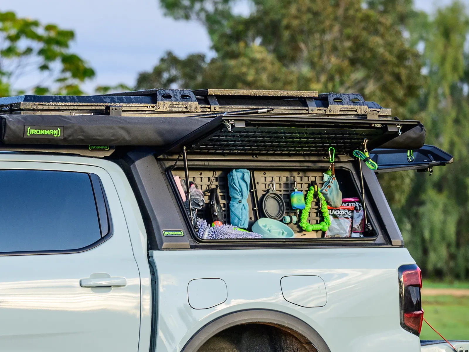 An open canopy window showing camp gear organised on a storage panel, with an awning and roof platform above